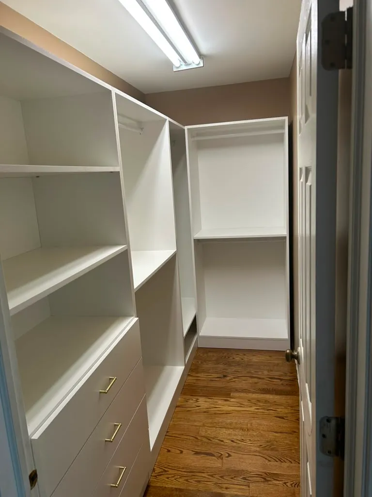 Finished walk-in closet with custom shelving, drawers, and brass hardware